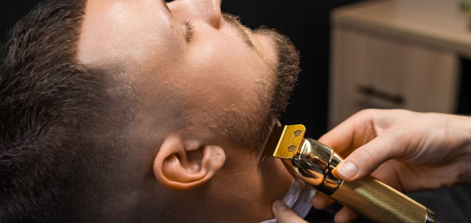 Barber,shearing,beard,to,man,in,barbershop,,close,up.